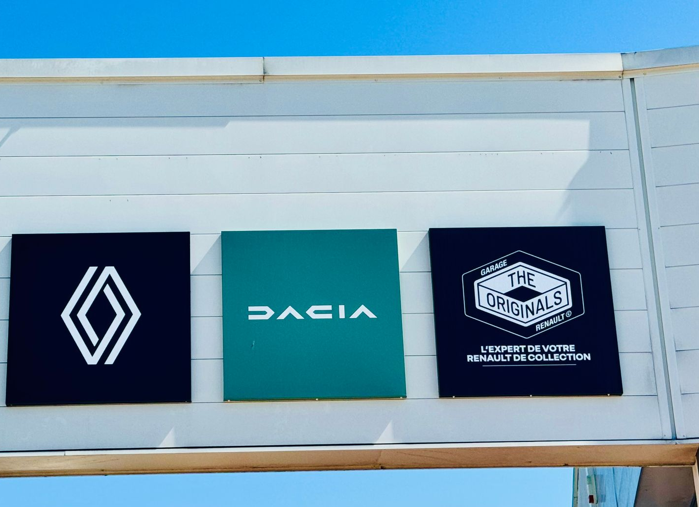 Trois logos carrés sur le mur blanc d'une concession : Renault, Dacia et The Originals.