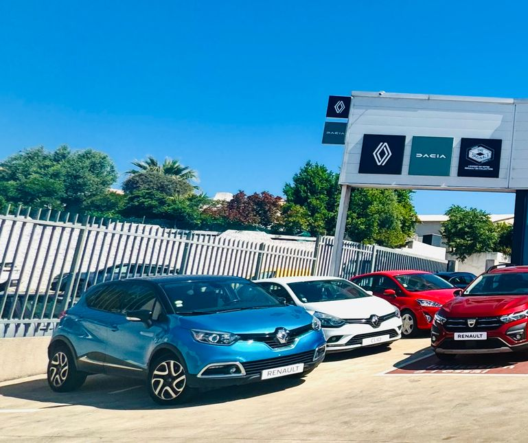 Parking d'une concession Renault avec plusieurs voitures garées sous un ciel dégagé.