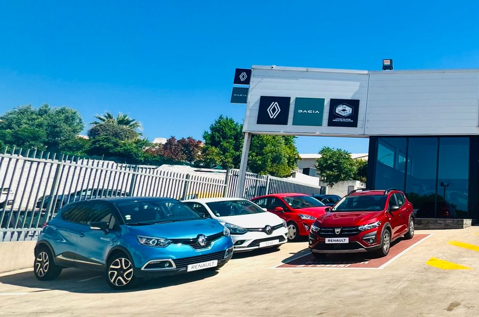Parking d'une concession Renault avec plusieurs voitures garées, sous un ciel d'un bleu éclatant.