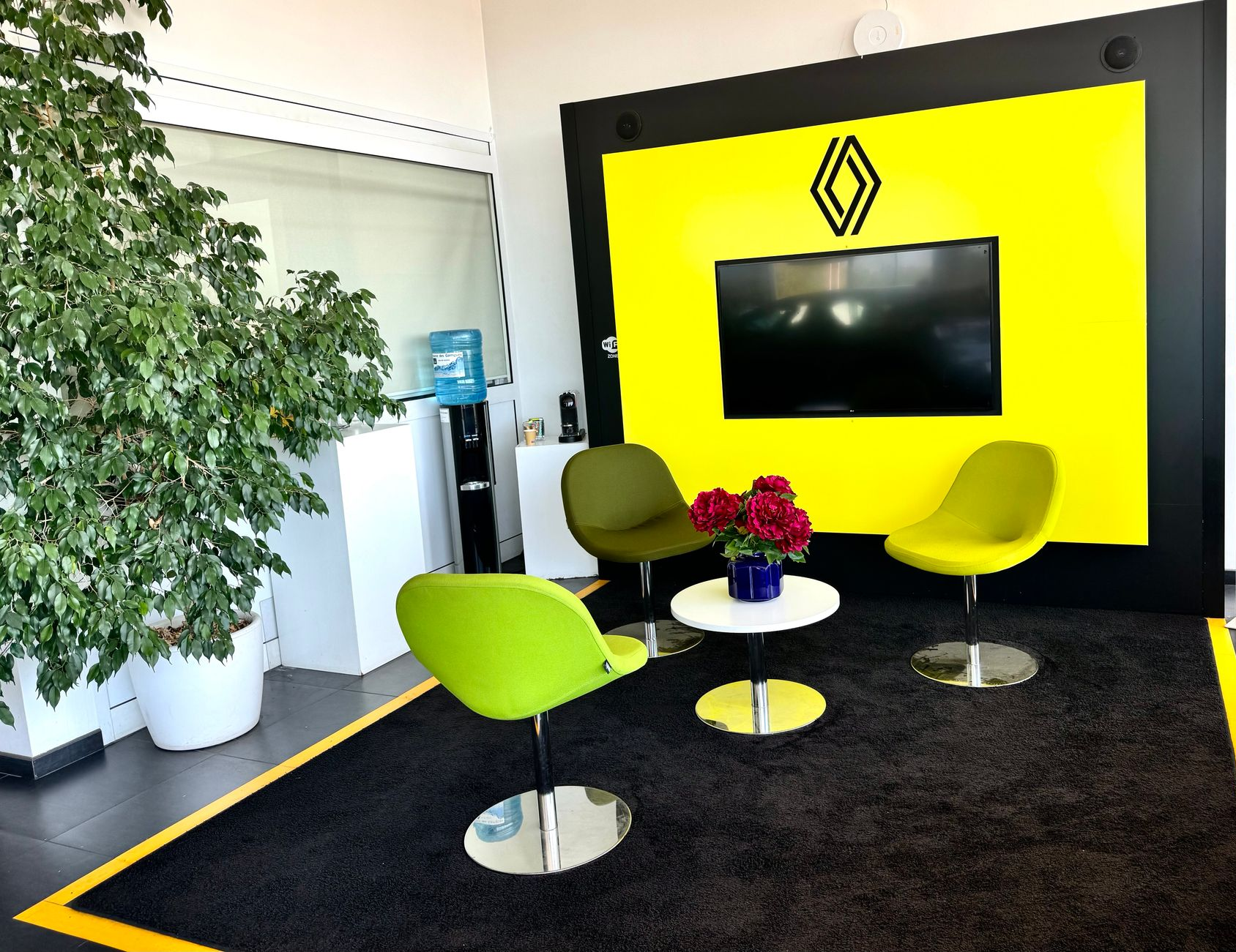 Accueil avec fauteuils, moquette noire, mur jaune et télévision dans une concession Renault.