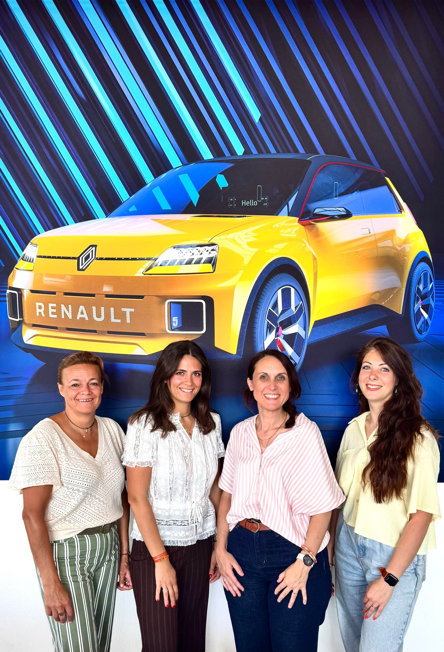 Quatre jeunes femmes se tiennent devant une affiche représentant une Renault jaune.