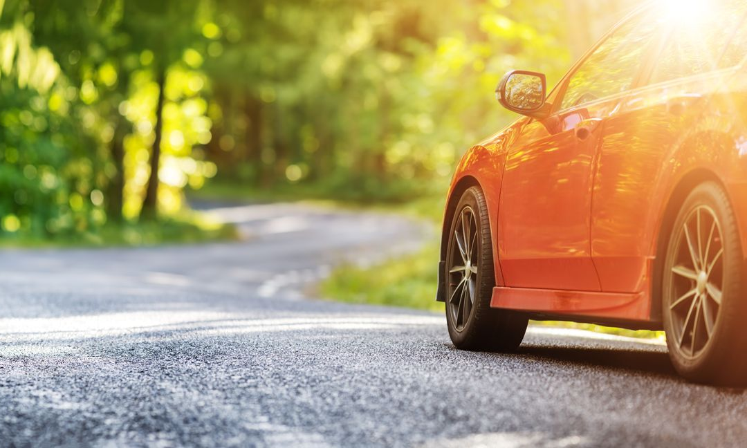 Voiture orange sur une route sinueuse ensoleillée avec des arbres en arrière-plan.