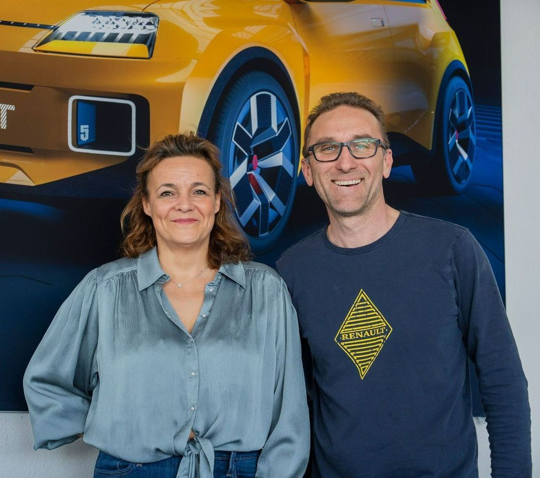 Deux personnes souriantes se tiennent devant l'affiche d'une Renault électrique jaune.