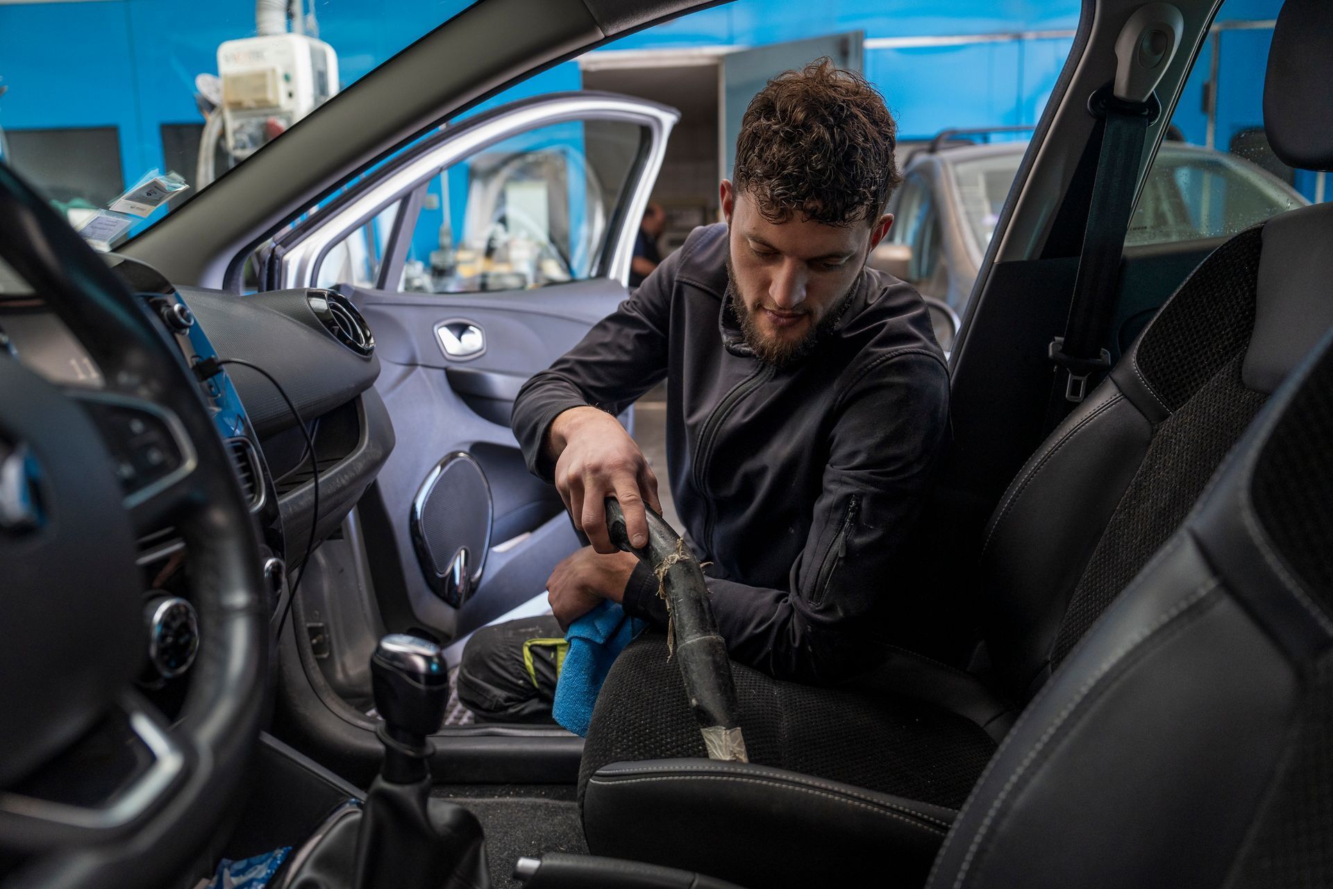 Un homme passe l'aspirateur sur le siège avant d'une voiture dans un garage.