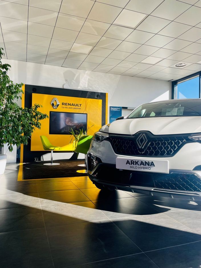 Renault Arkana blanche dans un showroom lumineux avec présentoir Renault jaune.
