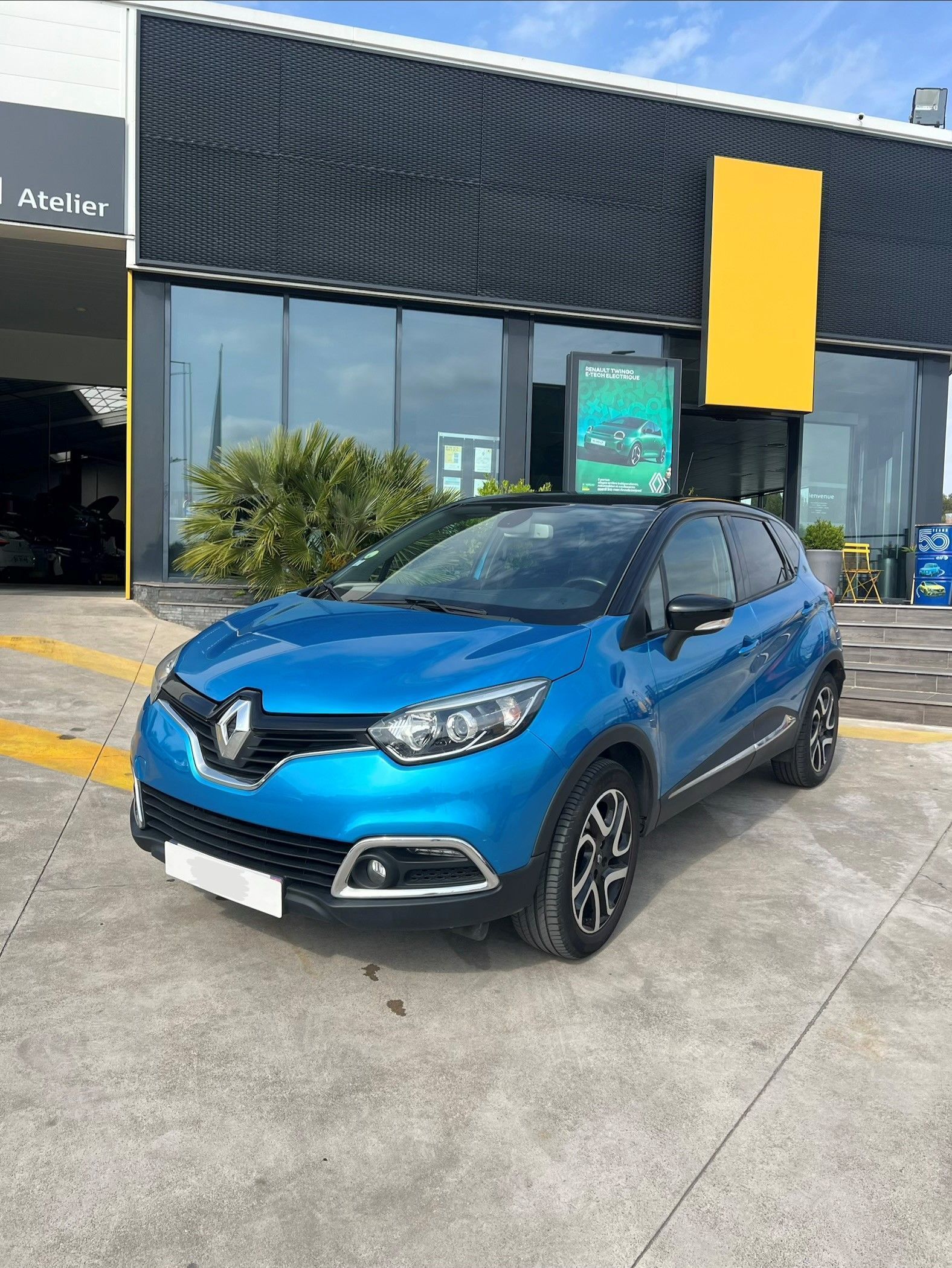 Une Renault Captur bleue est garée devant l'entrée de la concession.