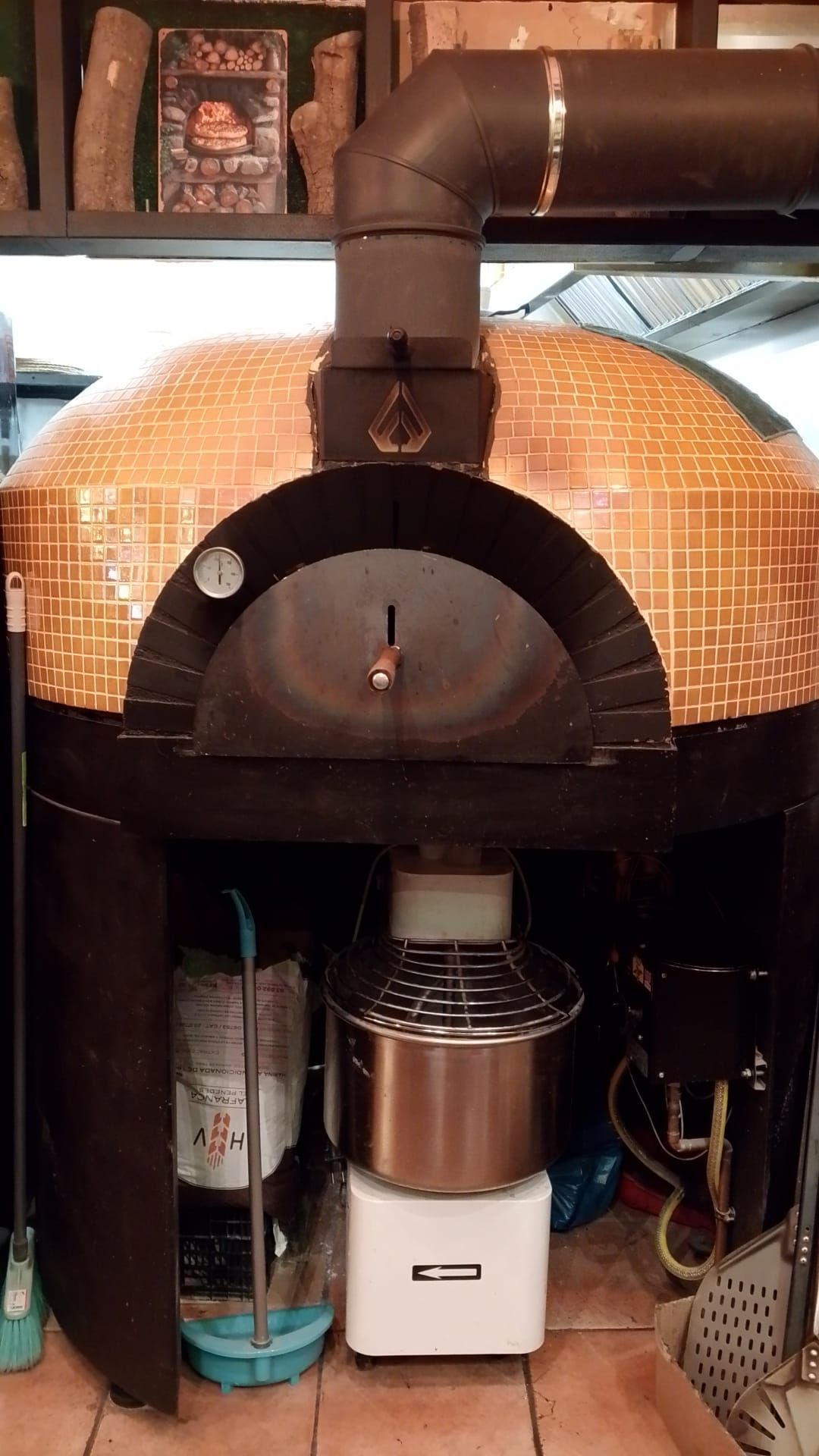 Un gran horno de pizza con forma de cúpula, revestido de azulejos y con una chimenea metálica