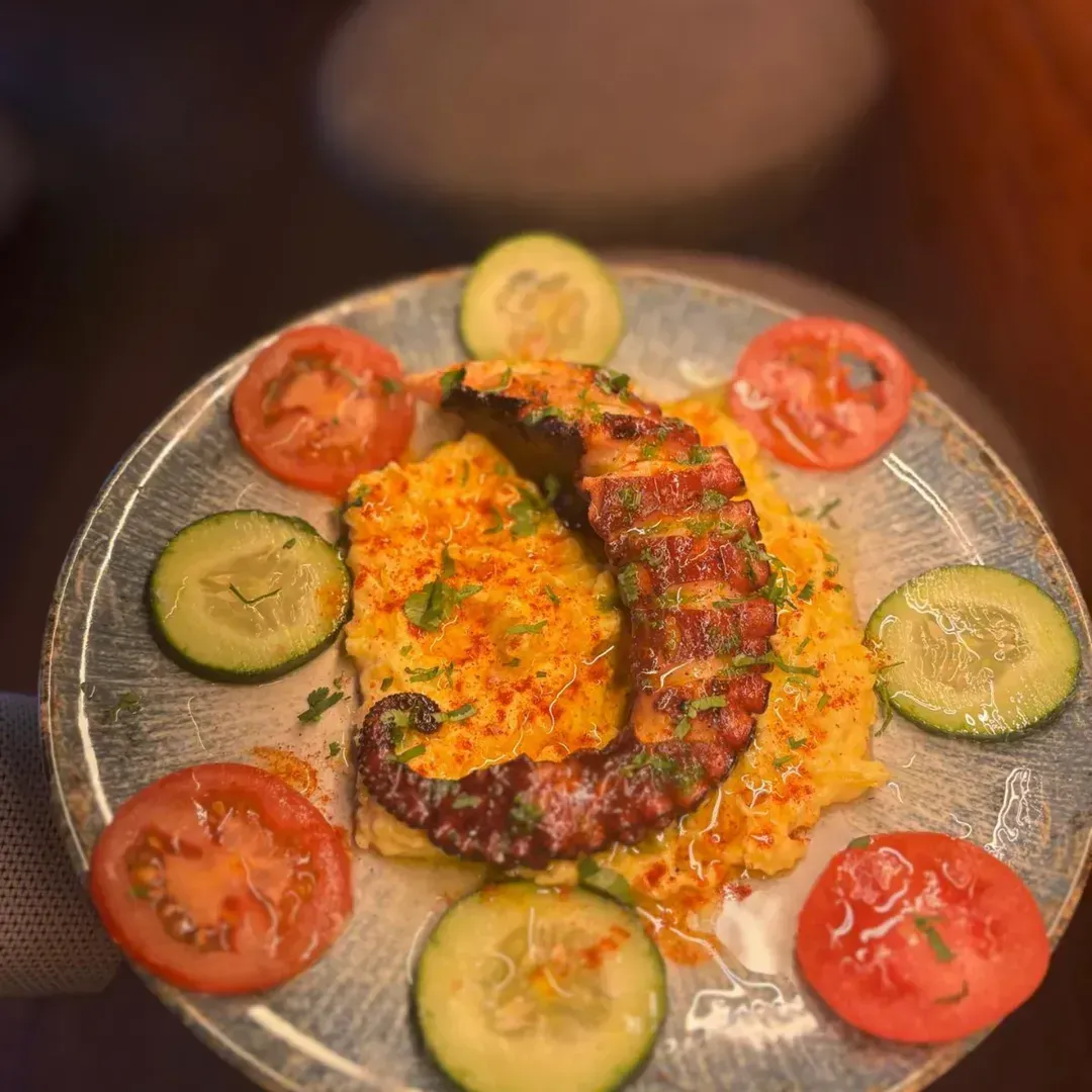 Un tentáculo de pulpo a la parrilla servido sobre polenta amarilla en un plato redondo