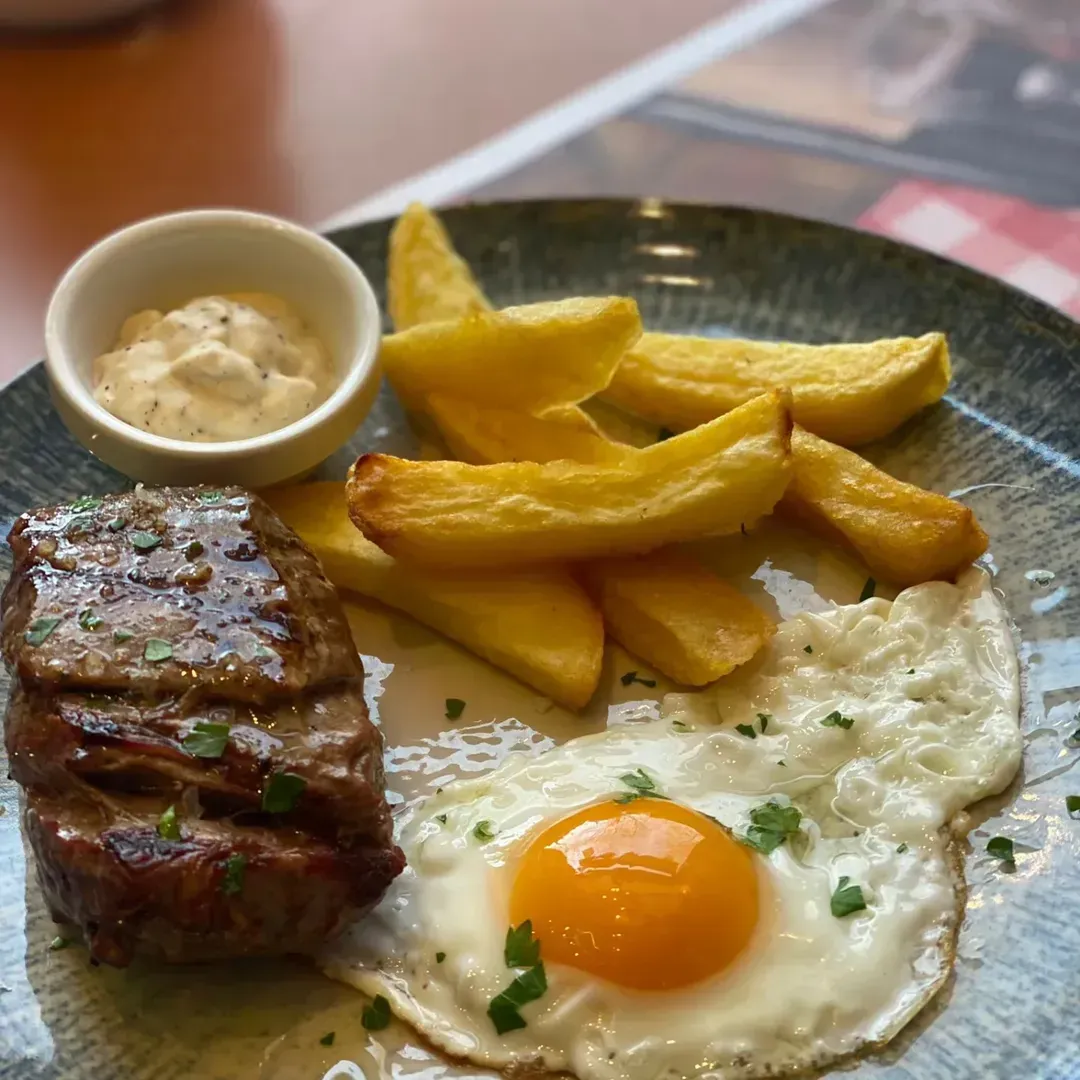 Un filete, un huevo frito y patatas fritas gruesas servidos en un plato con estampado azul