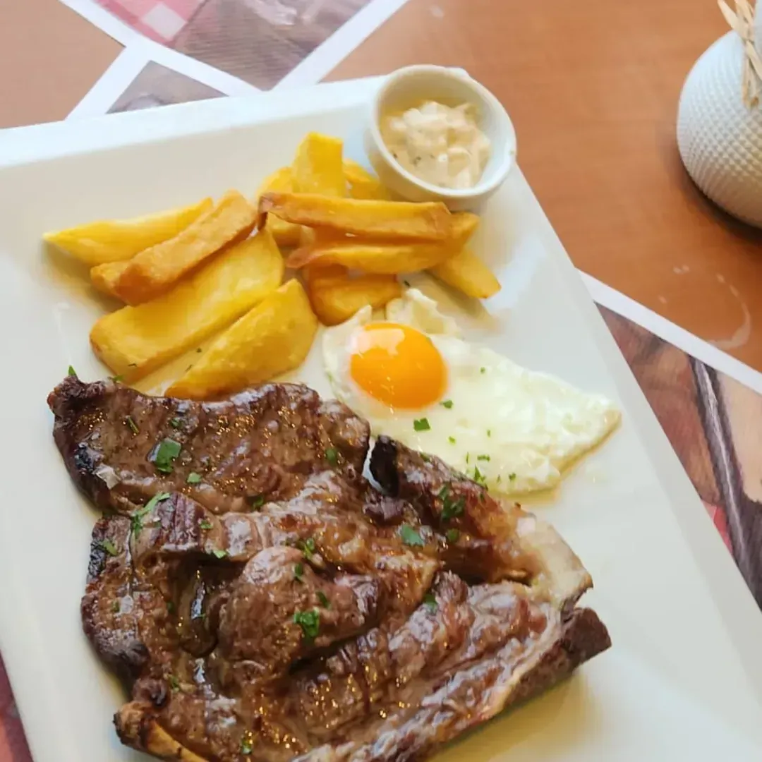Un filete a la parrilla servido en un plato blanco con patatas fritas en gajos