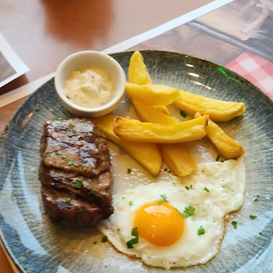 Un plato que incluye un filete a la parrilla, un huevo frito con la yema líquida, patatas gajo cortadas en rodajas gruesas