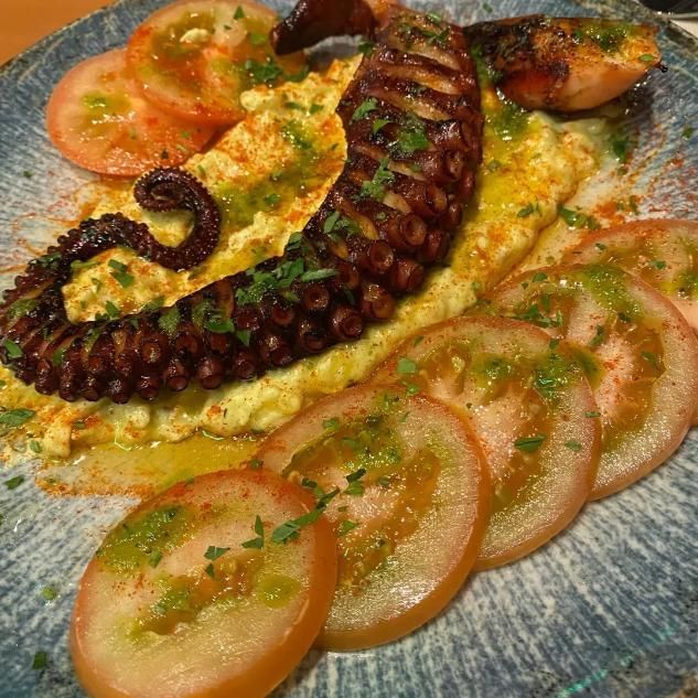 Tentáculo de pulpo a la parrilla servido sobre un puré cremoso, adornado con hierbas frescas