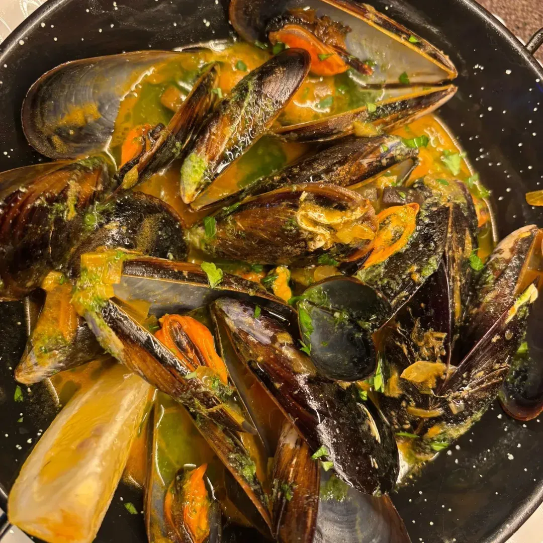 Una porción de mejillones en un sabroso caldo de color naranja con hierbas y una rodaja de limón