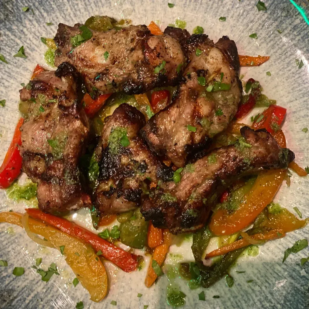 Trozos de carne a la parrilla servidos con coloridas tiras de pimiento salteado en un plato estampado de color claro.