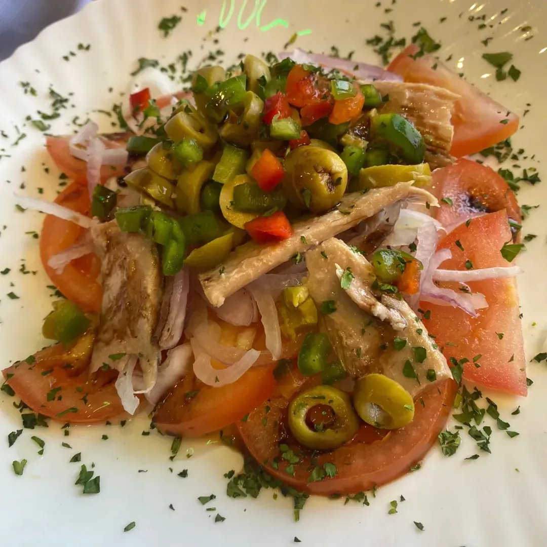Un plato de ensalada de tomate fresco cubierta con aceitunas verdes en rodajas, pimientos rojos