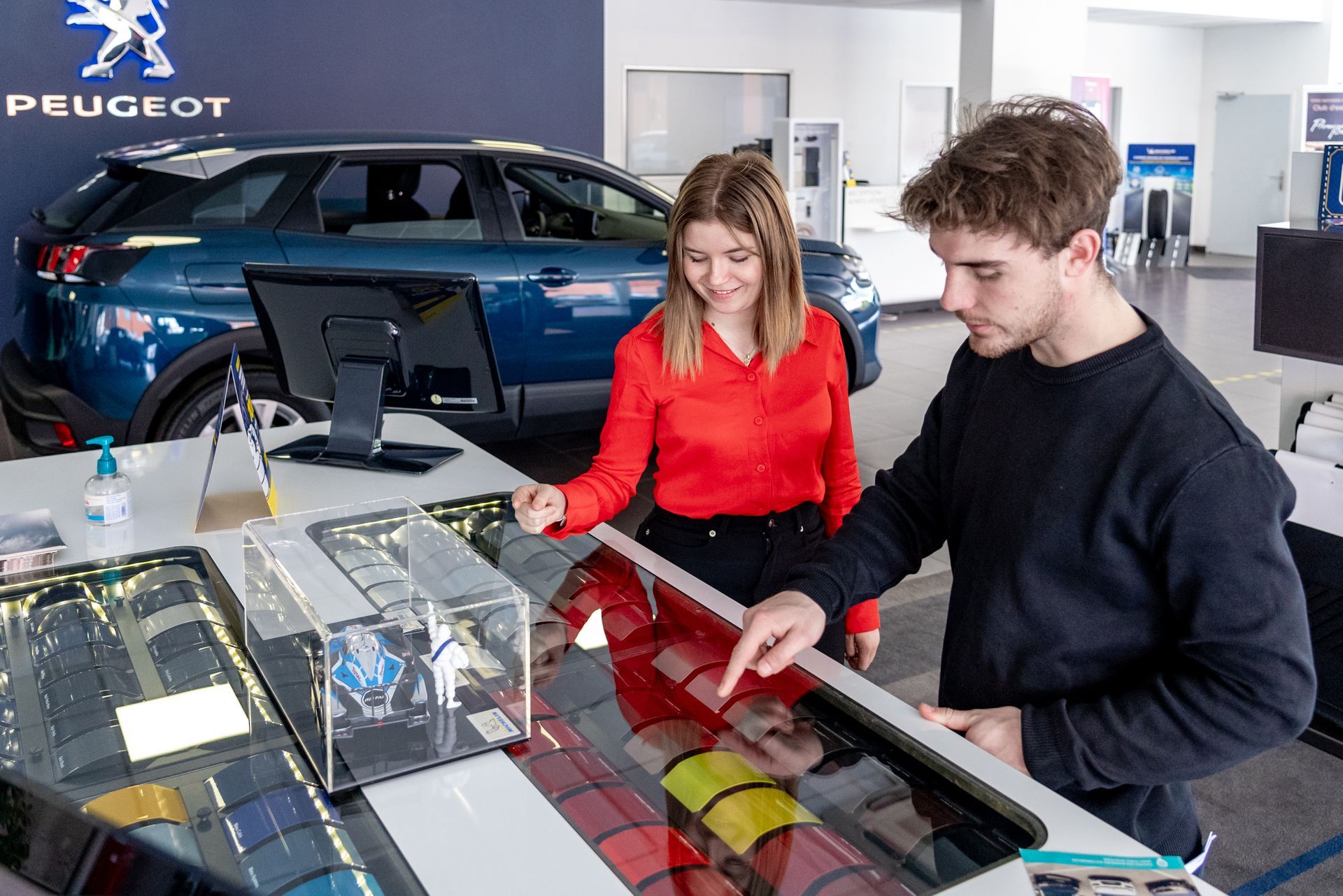 Deux personnes regardent une vitrine avec des échantillons de couleurs de peinture pour véhicules