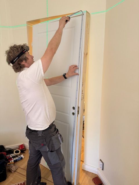 Valkoiset pariovet johtavat vaaleanvihreään rakennukseen, jossa on pienet ikkunat, valkoiset ruukut ja ulkona kahvilatyyli.