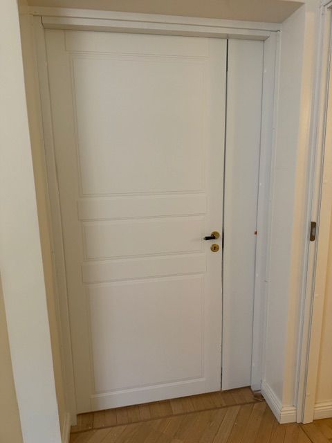 Luonnonvalkoiset pariovet, joissa on upotetut paneelit ja yhteensopivat messinkiset vetimet, jotka on asetettu kulmaan.