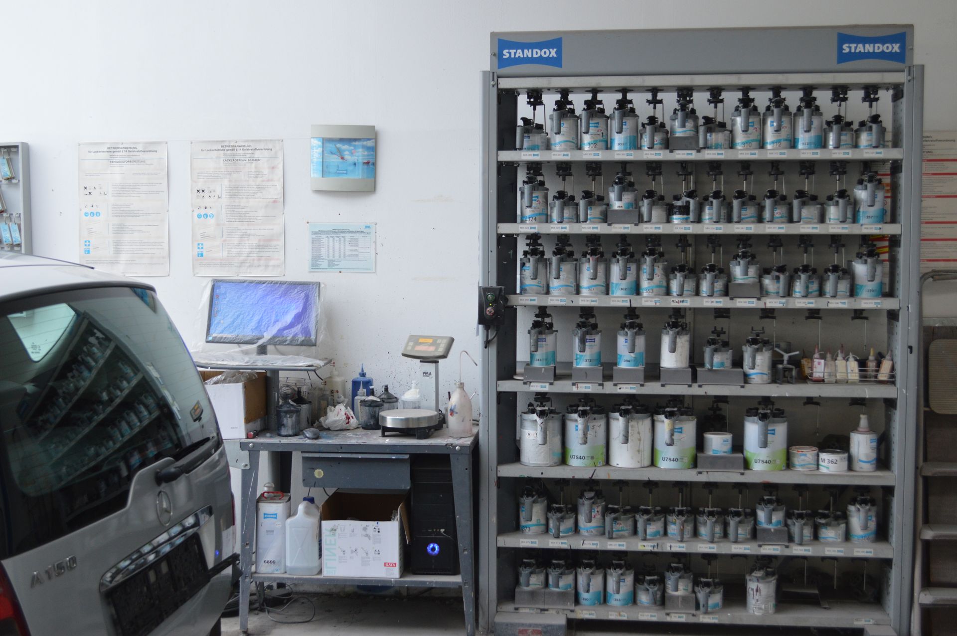 Farbmischstation in der Werkstatt mit Regalen voller Lackdosen und Computerarbeitsplatz