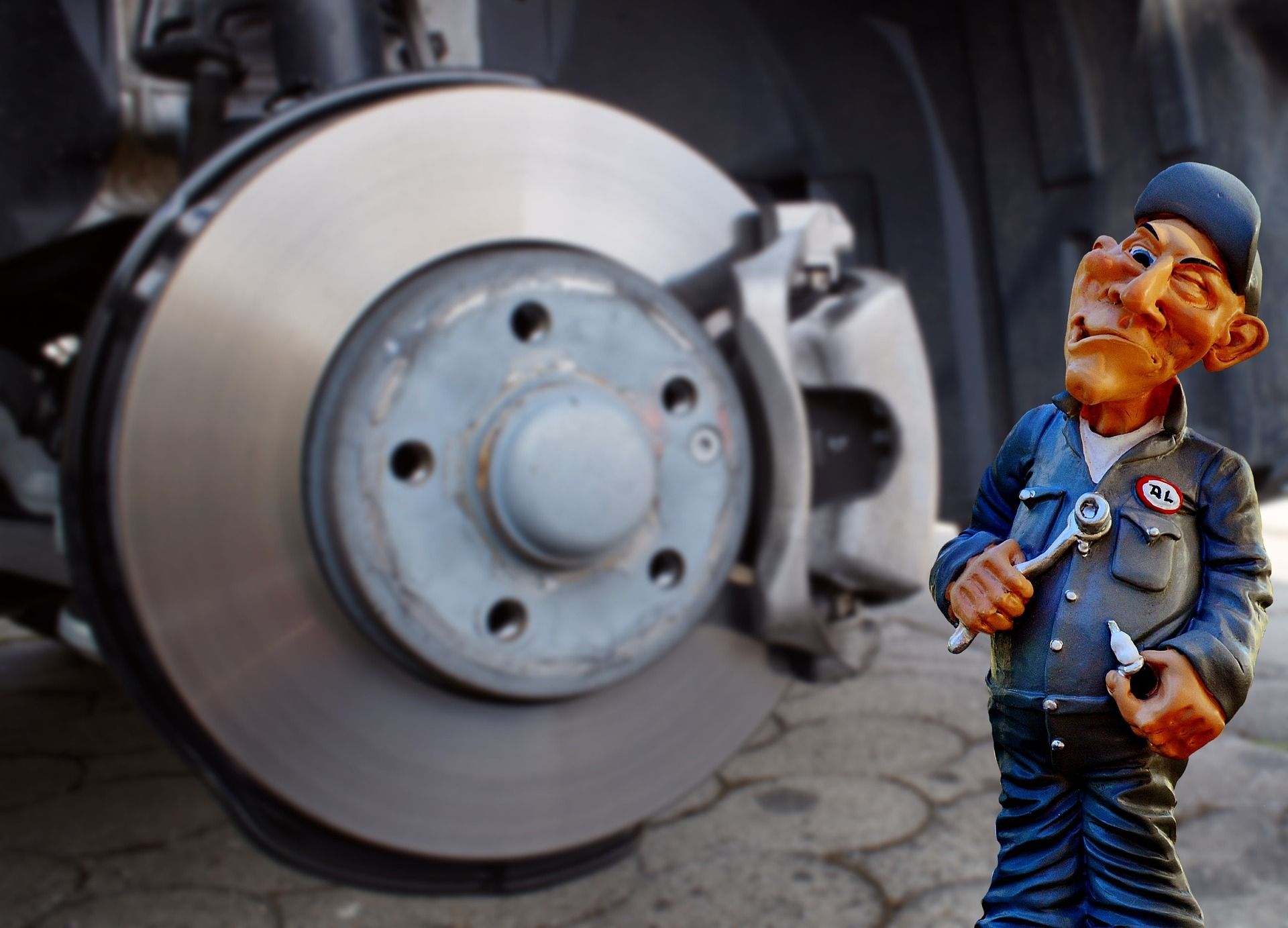 Nahaufnahme einer Autoscheibenbremse mit einer kleinen Mechanikerfigur davor.