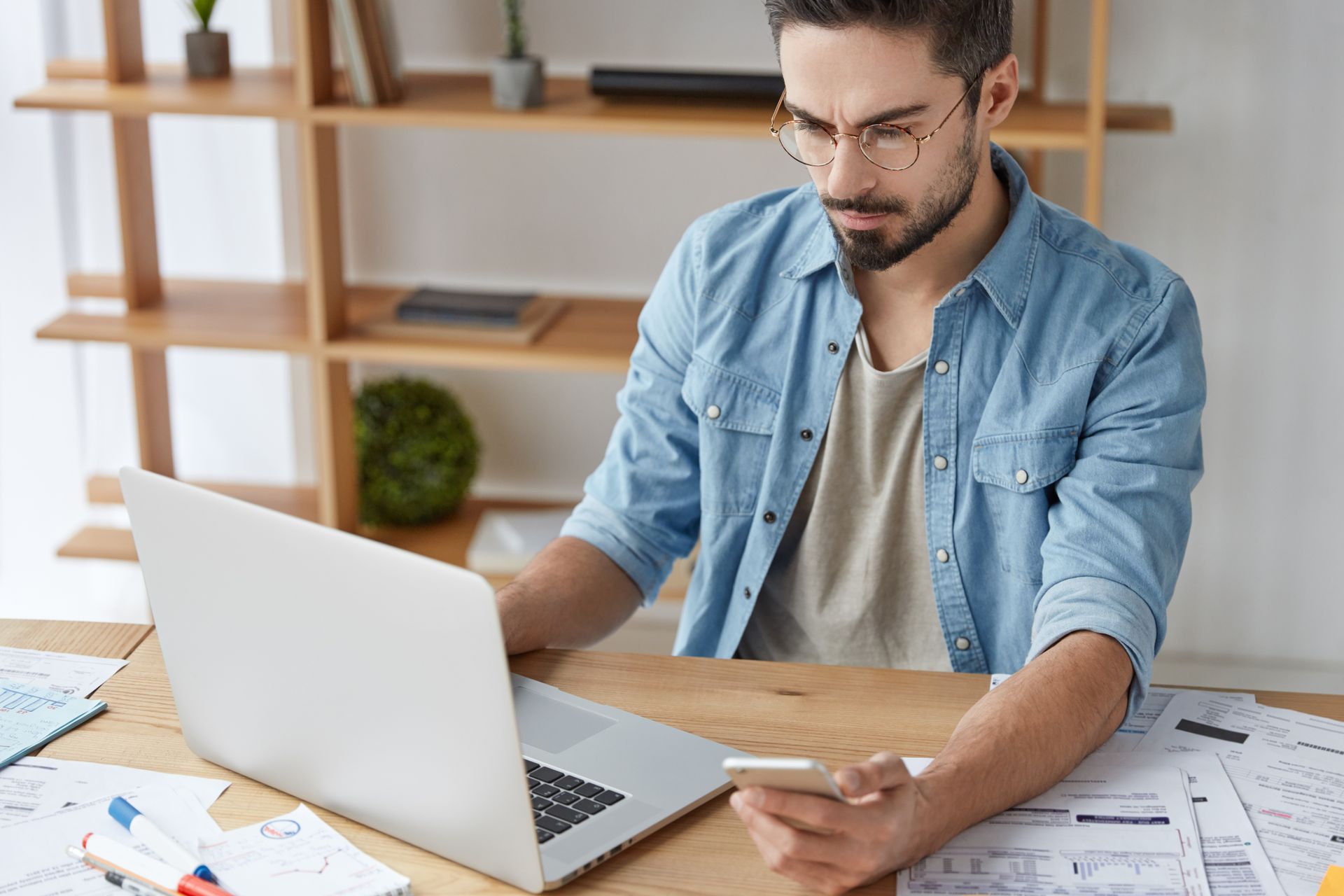 Un homme devant son ordinateur regarde son téléphone portable