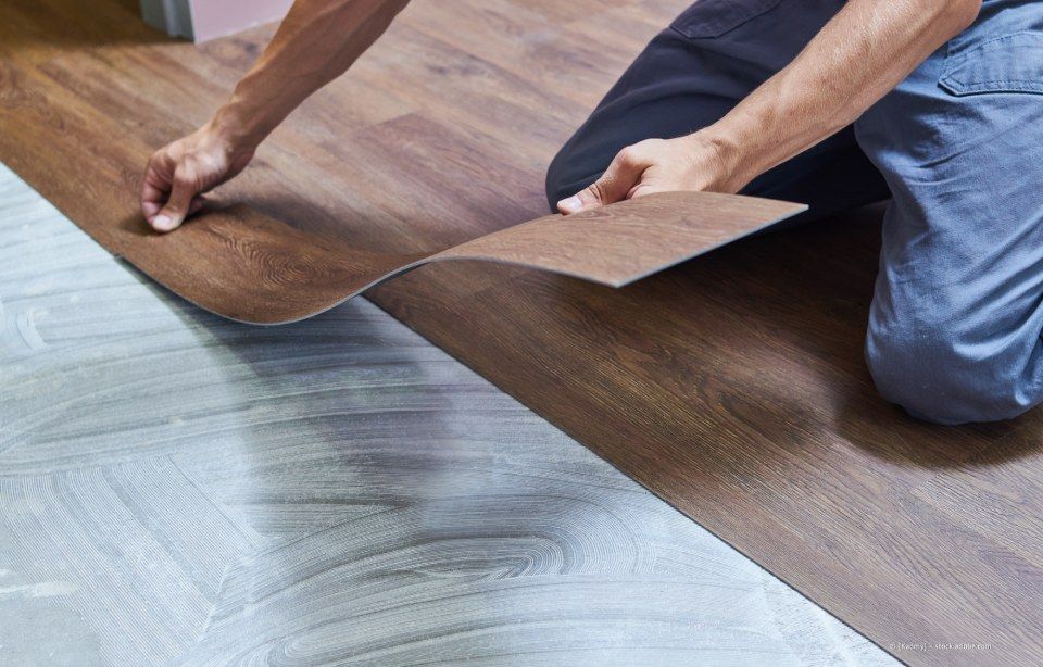 Person verlegt einen braunen Vinylboden in Holzoptik über einer grauen Unterlage