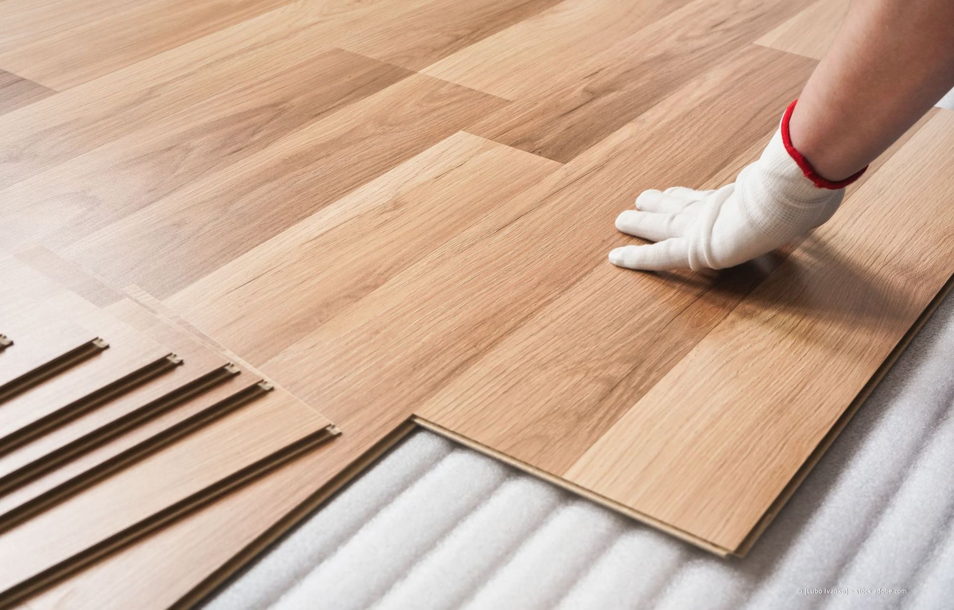 Handschuhbewehrte Hand verlegt hellen Holzlaminatboden auf Unterlage