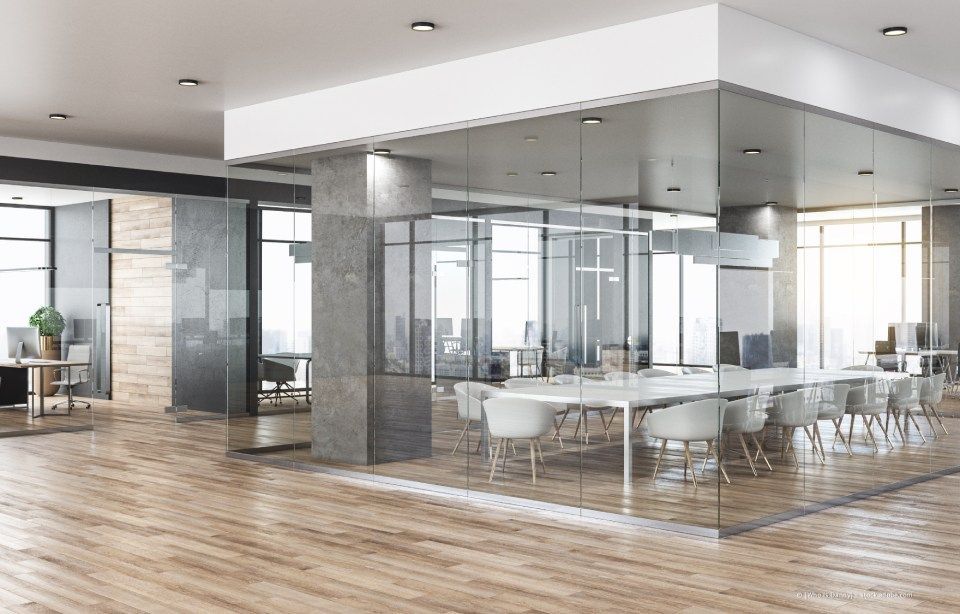 Moderne Bürolobby mit verglastem Konferenzraum, Holzböden und weißen Tischen und Stühlen