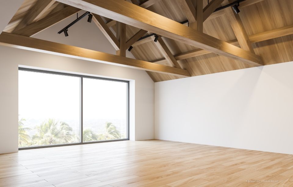 Helles, leeres Loft mit freiliegenden Holzbalken, weißen Wänden und einer großen Glasschiebetür.