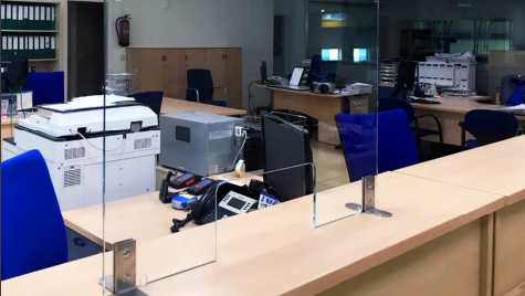 Un área de recepción en una oficina con una barrera de vidrio entre los escritorios y las sillas.