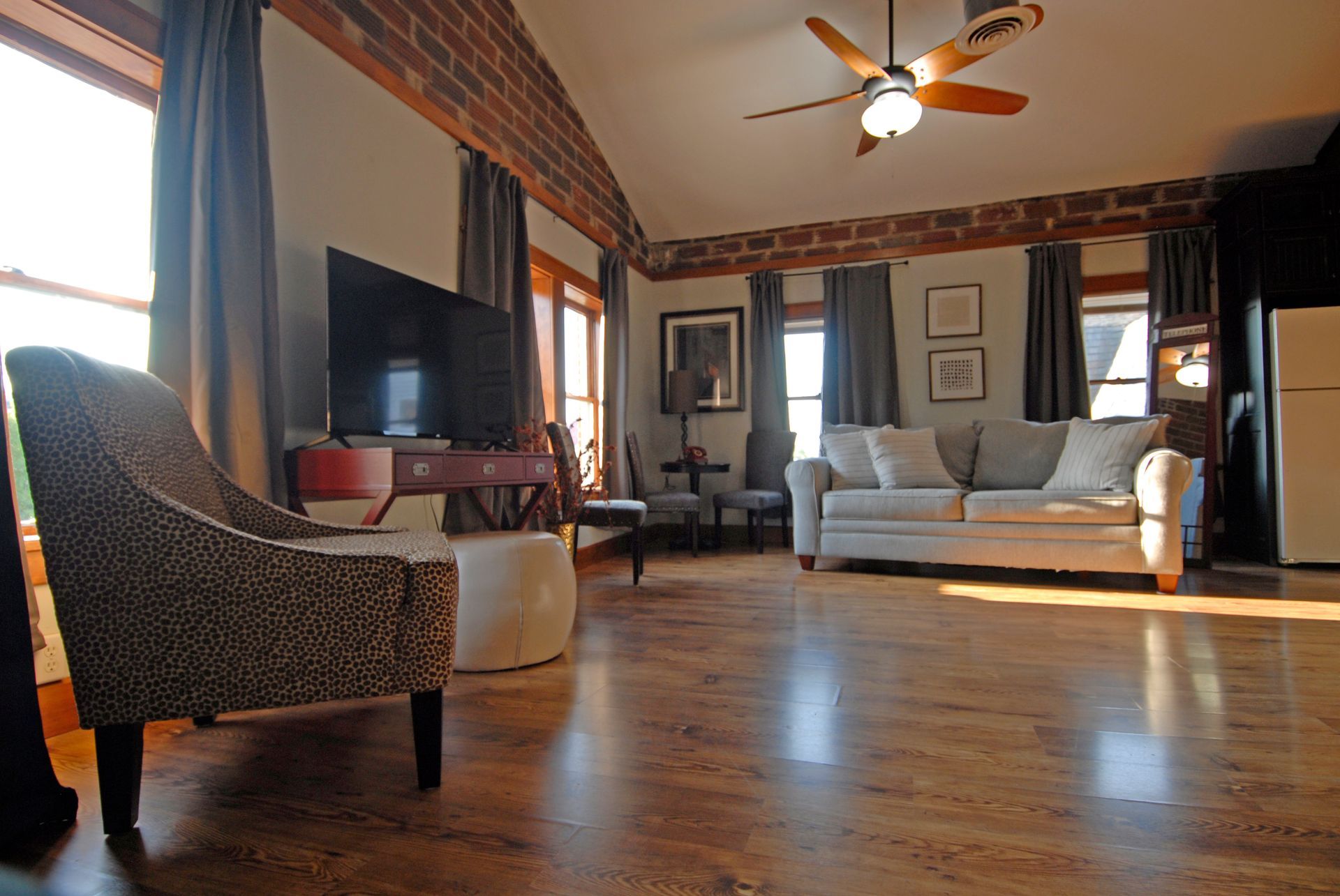 A living room with a couch , chair , television and ceiling fan.