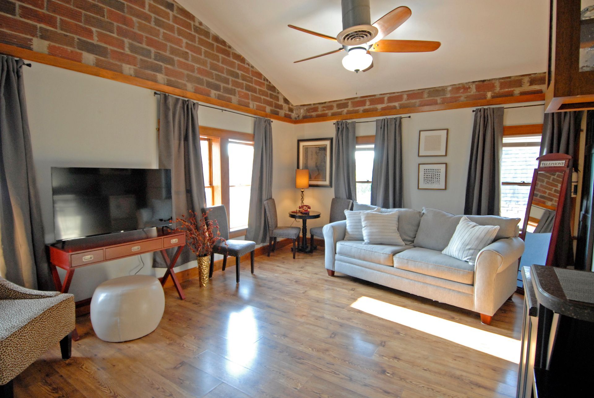 A living room with a couch , chairs , a flat screen tv and a ceiling fan.