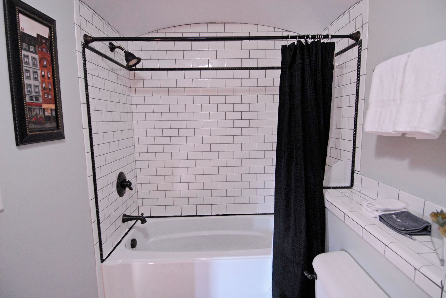 A bathroom with white tiles and a black shower curtain.