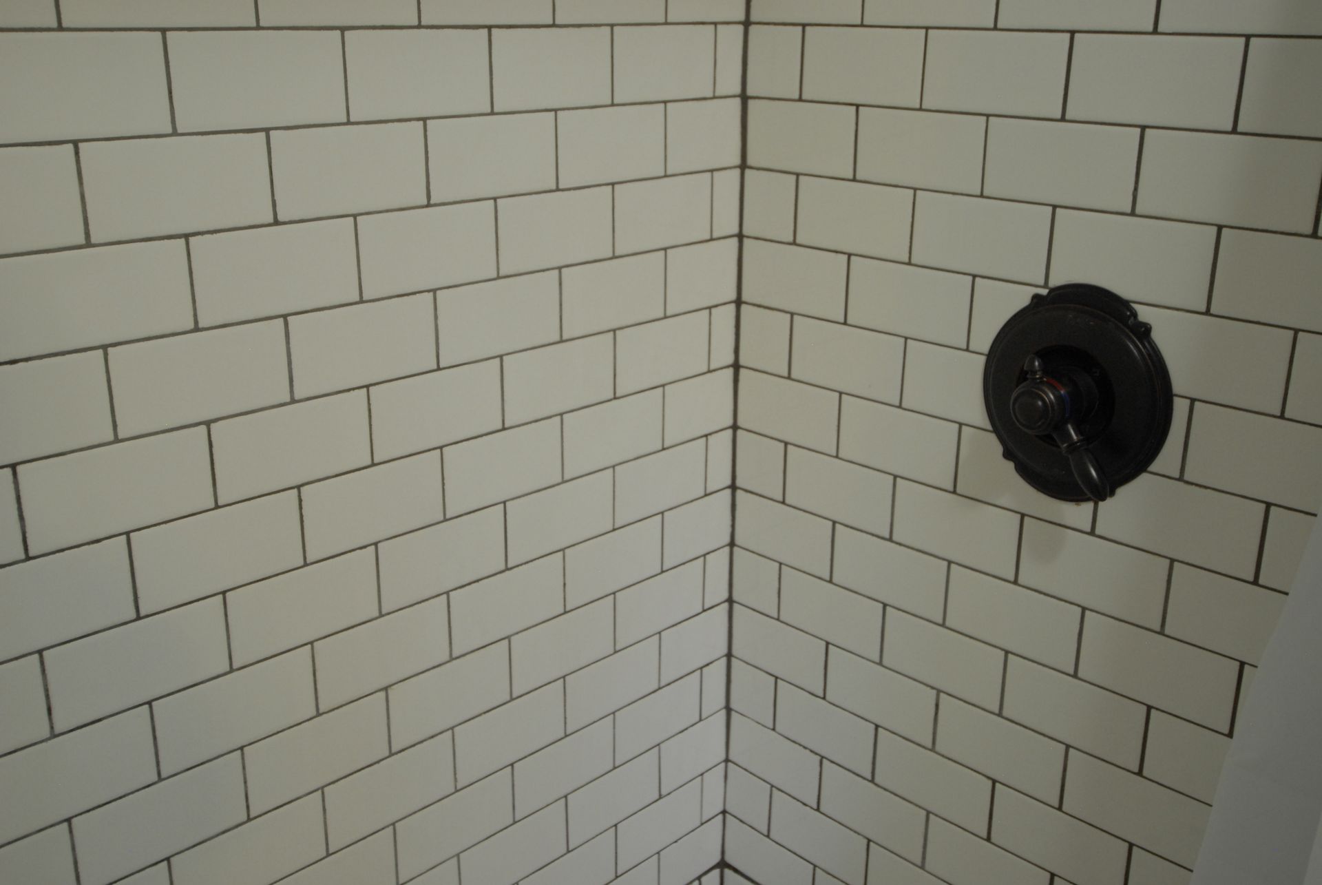 A shower stall with white tiles and a black shower head