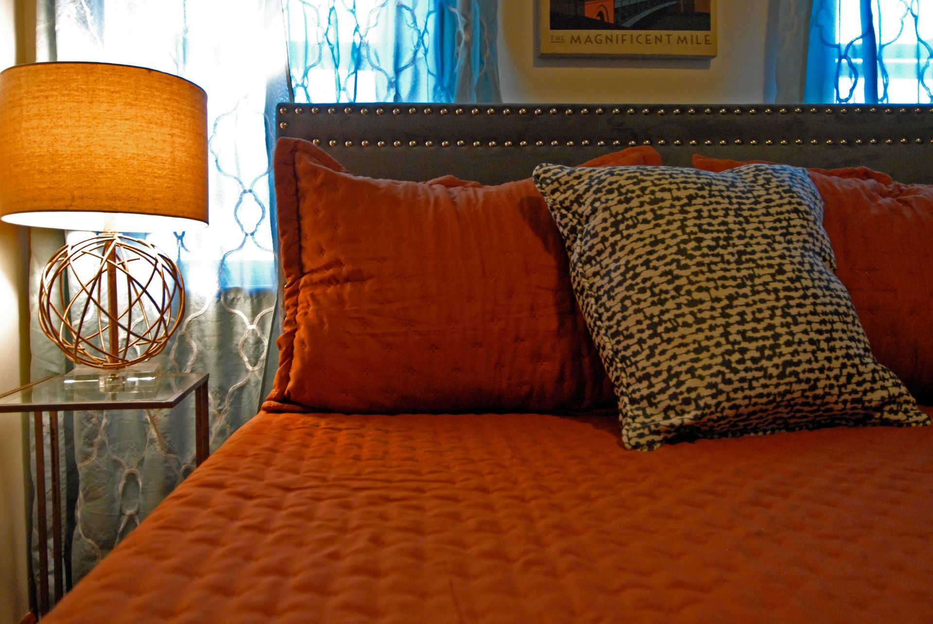 A bed with orange sheets and pillows next to a lamp