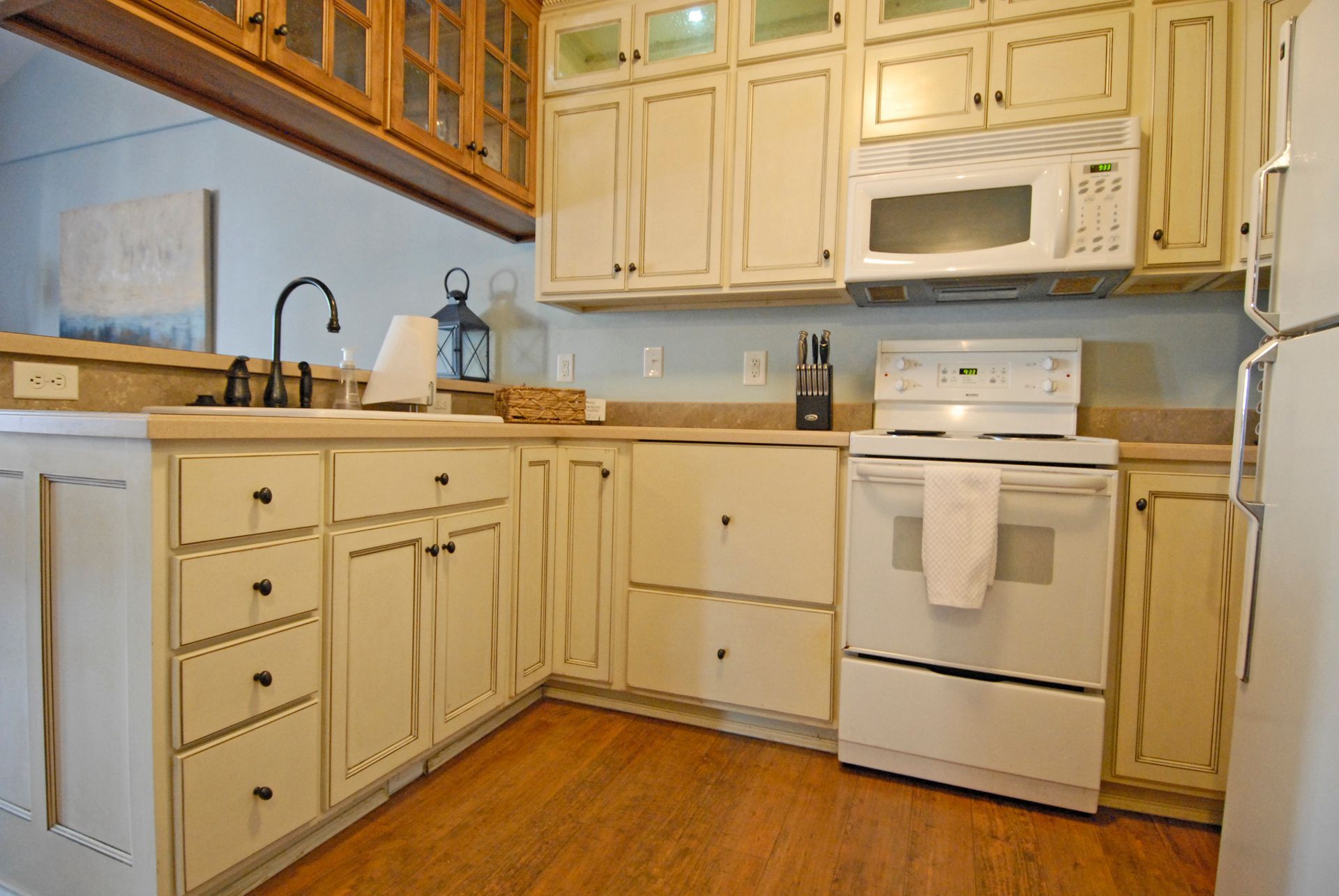 A kitchen with white cabinets , a stove , microwave , refrigerator and sink.