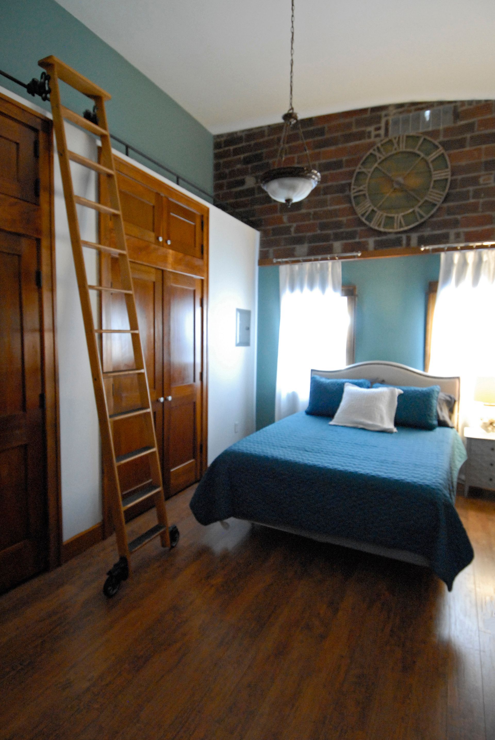 A bedroom with a bed a ladder and a clock on the wall