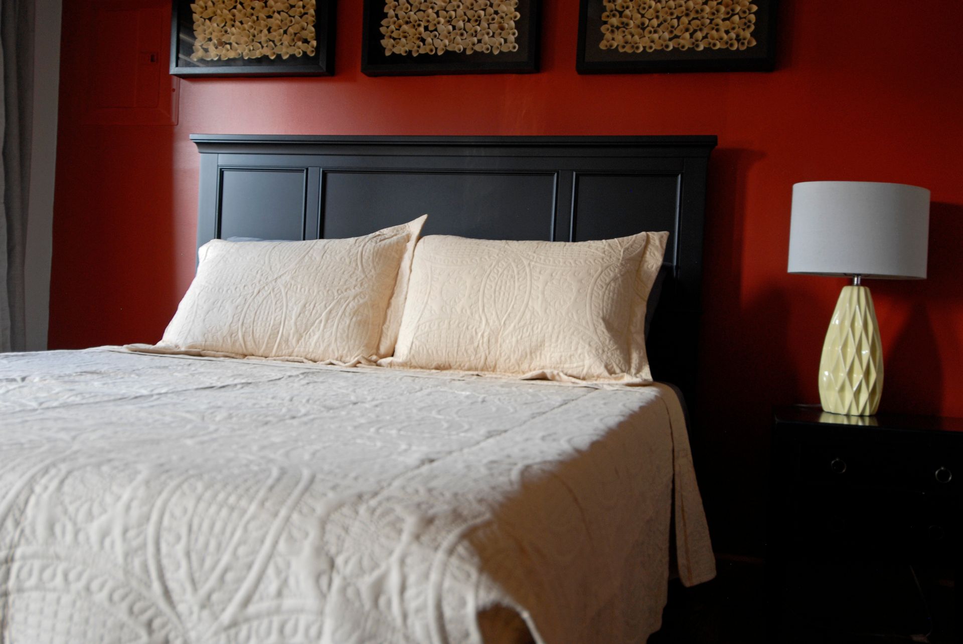A bed with white sheets and pillows in a bedroom with red walls