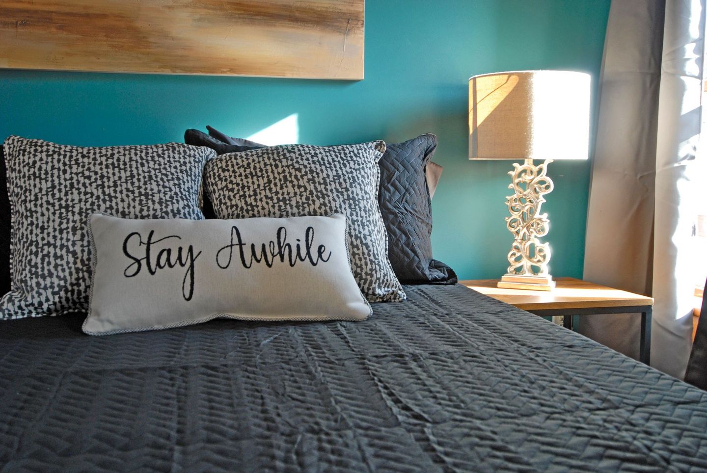 A bed with a pillow that says `` stay awhile '' on it.