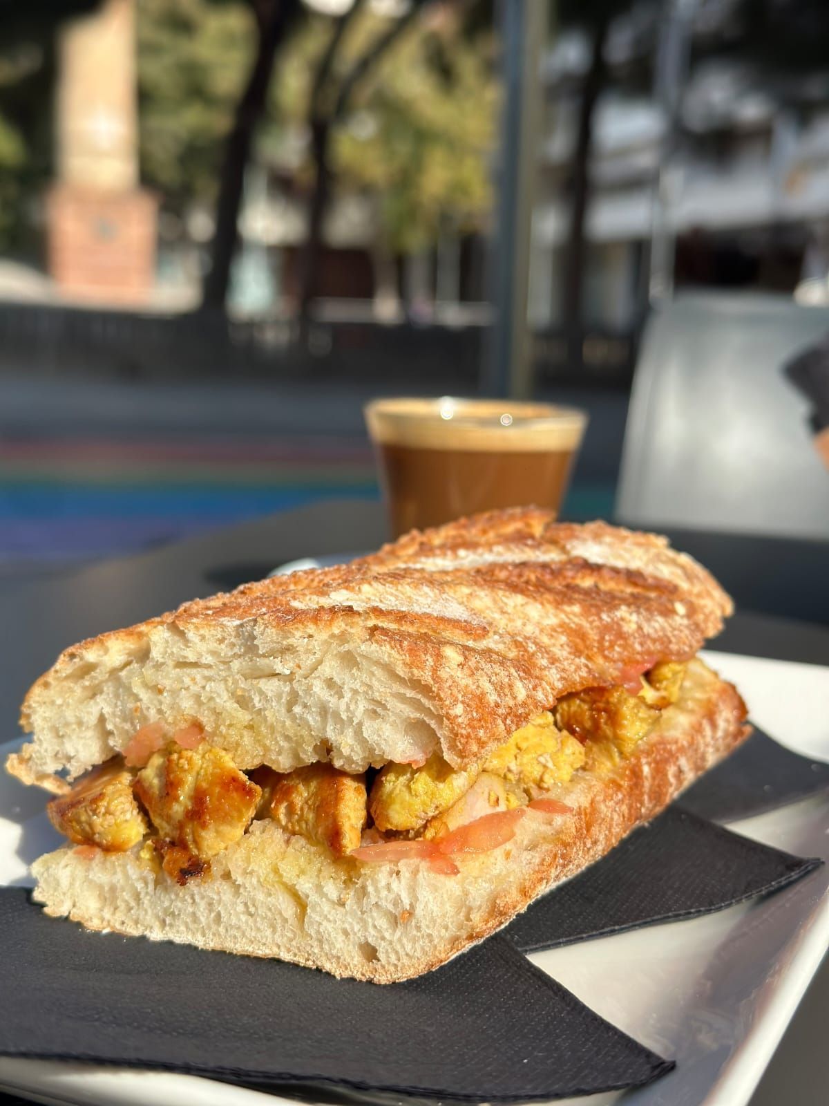 Un sándwich de baguette relleno de jamón servido en un plato con una pequeña taza de salsa roja.
