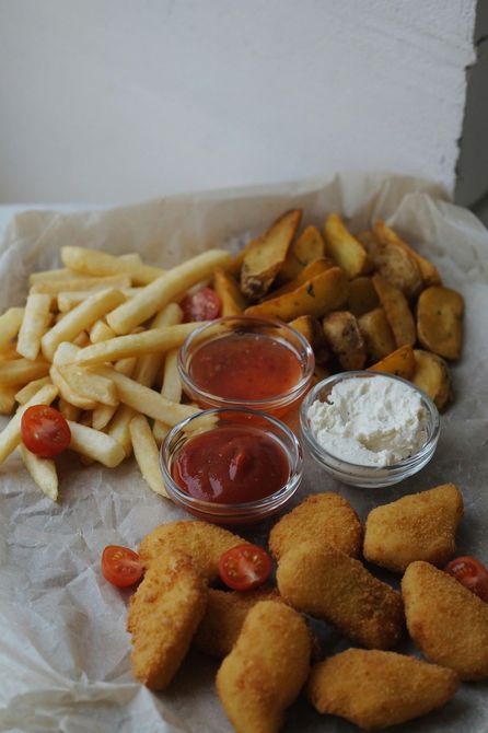 Papas fritas, papas gajo y nuggets de pollo con kétchup y crema agria sobre papel pergamino.