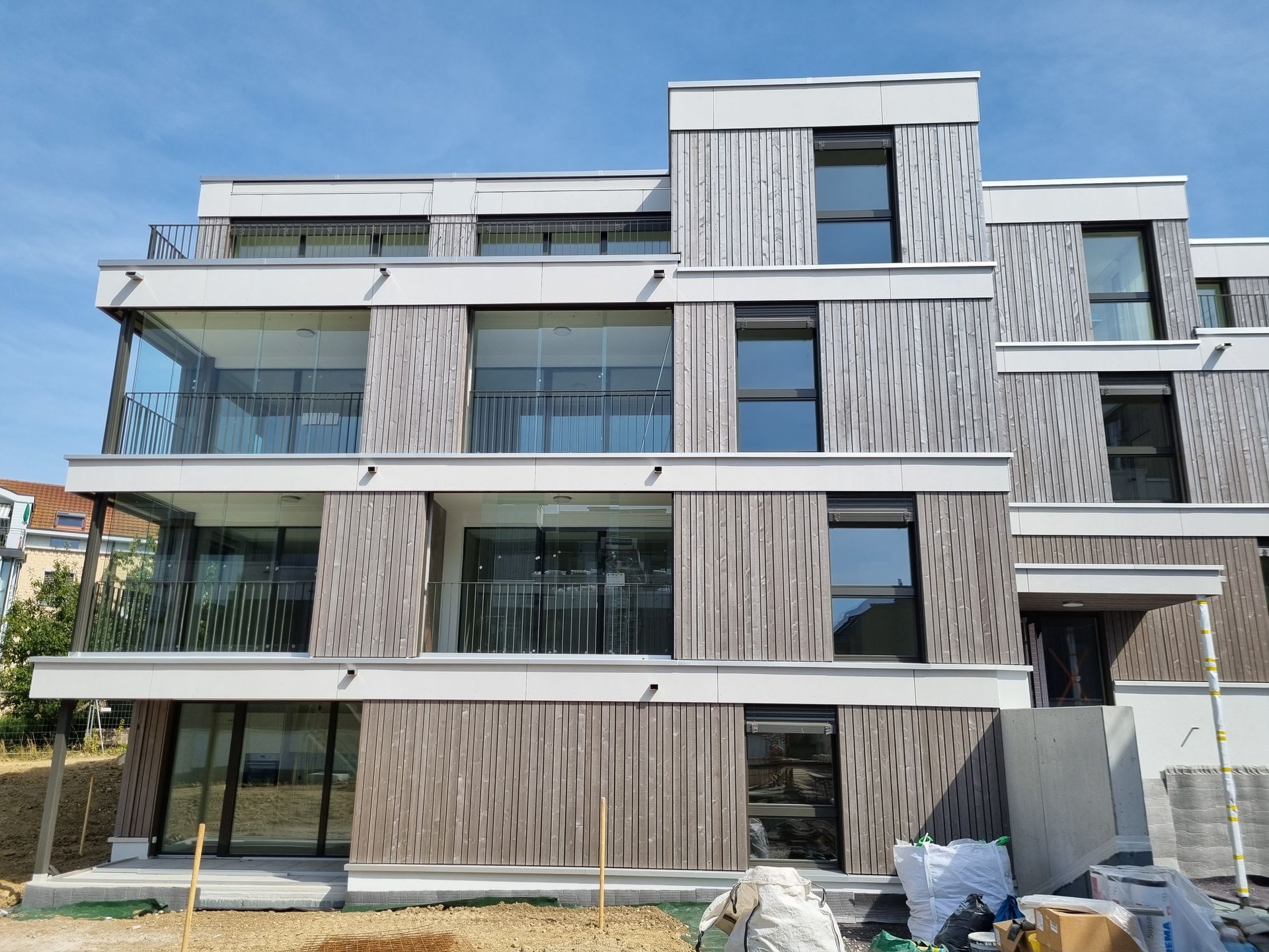 Modernes Mehrfamilienhaus mit Holzvertäfelung und Balkonen; klarer Himmel.