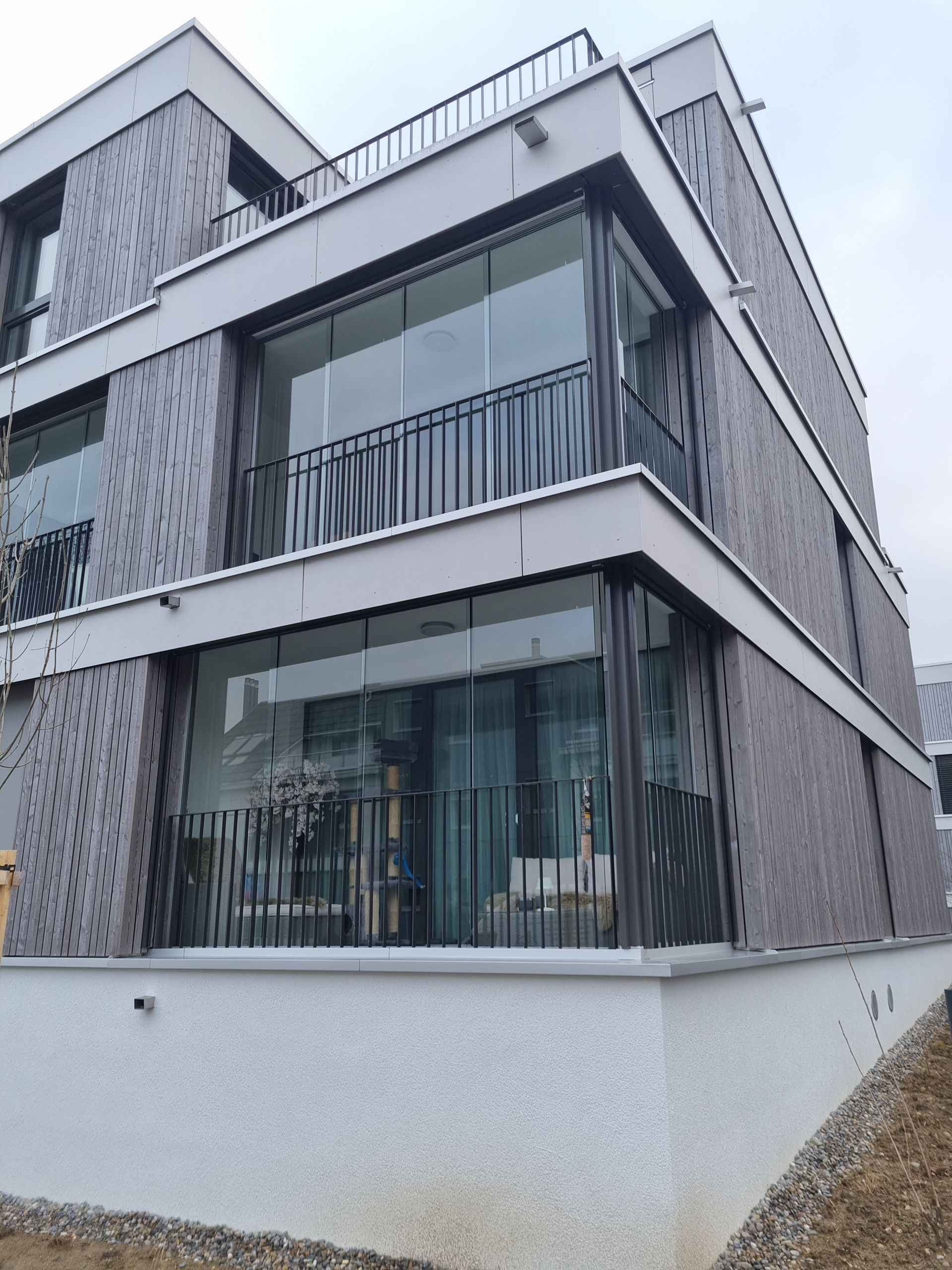 Modernes mehrstöckiges Gebäude mit Backsteinfassade, Glasbalkonen und dunklem Geländer.