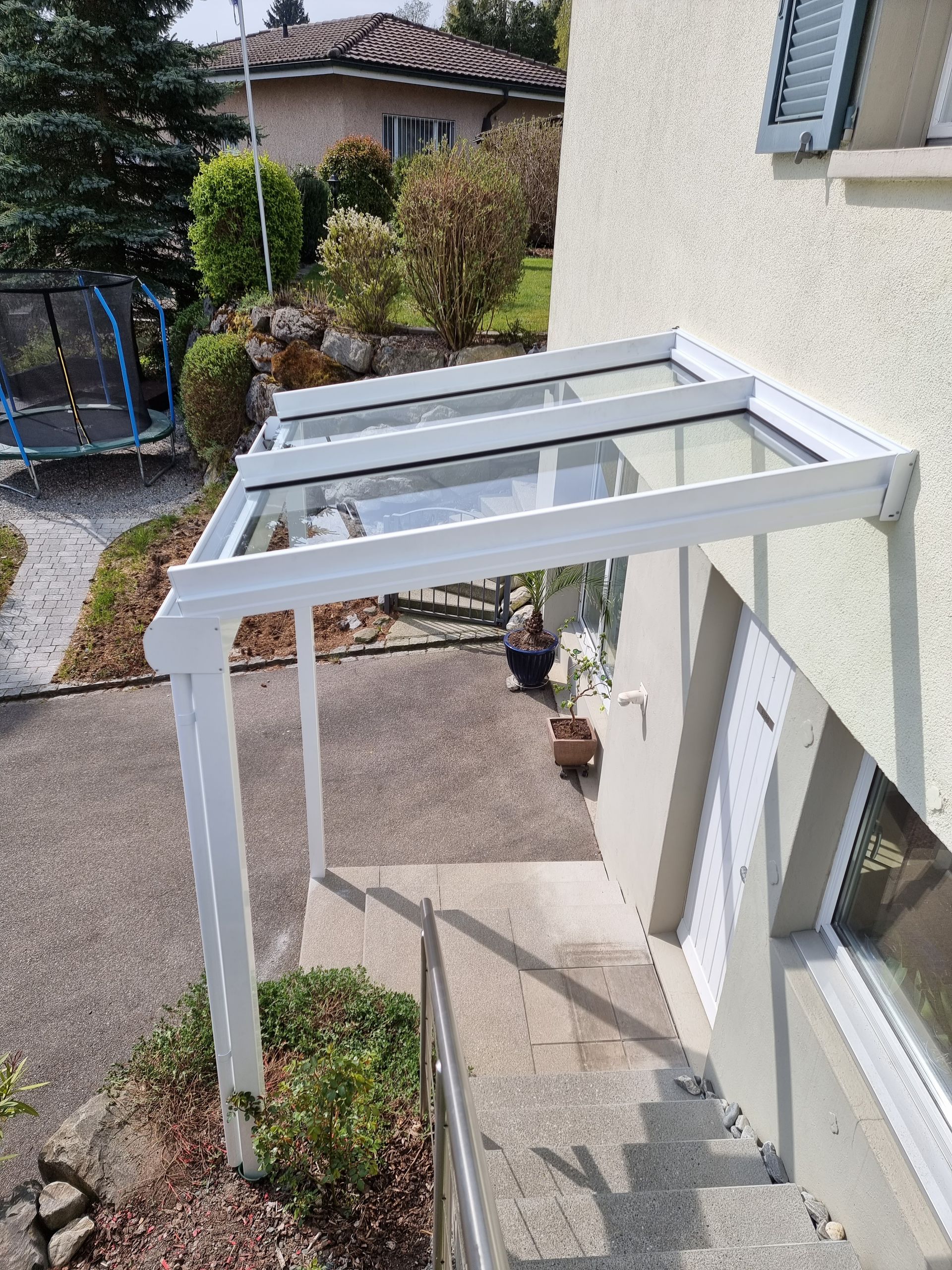 Weisse Markise über der Eingangstreppe. Glasdach, weisser Rahmen, Stufen führen zur Tür, sonniger Tag.