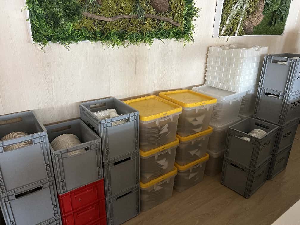 Contenedores de almacenamiento grises y amarillos apilados contra una pared con arte de musgo.