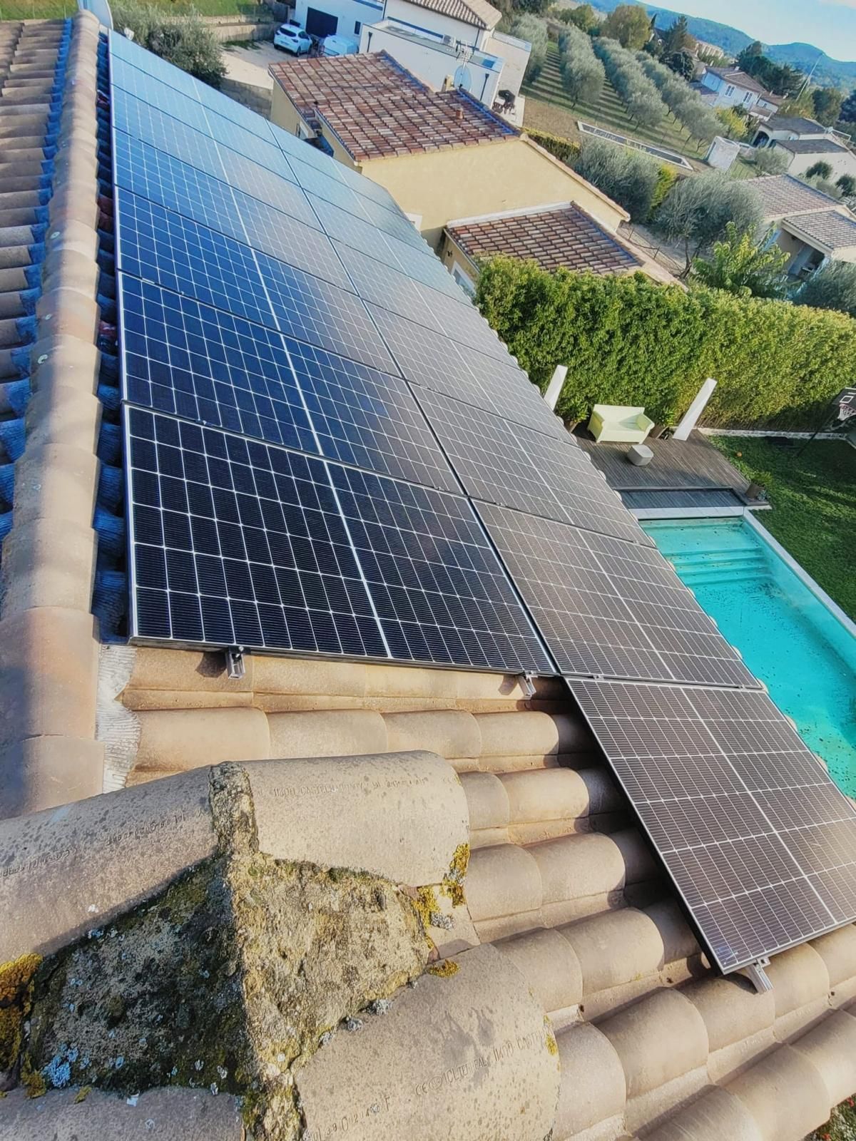 Vue en plongée d'une toiture avec panneaux solaires devant une piscine.
