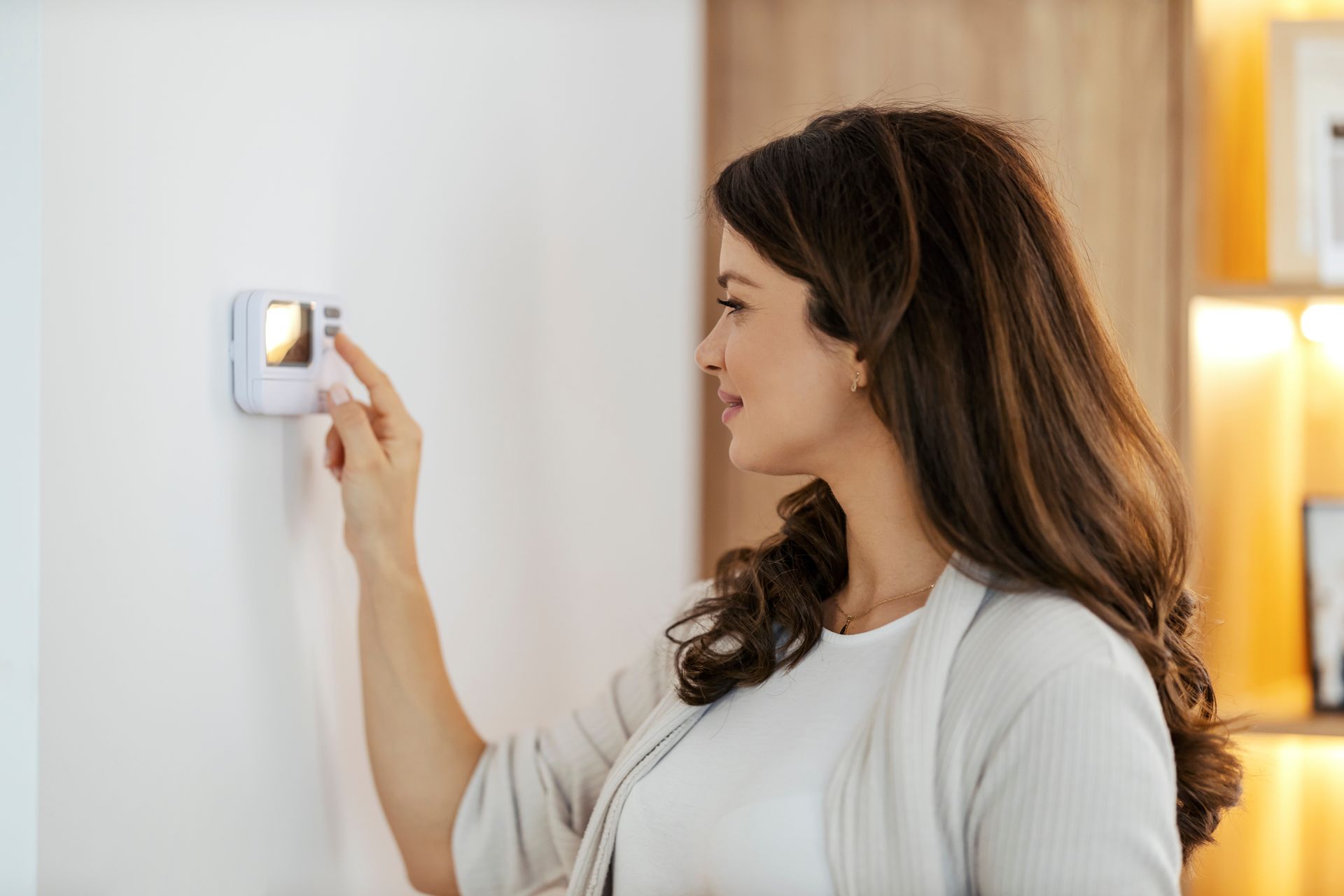 Une femme réglant la température à l'aide d'un thermostat mural.