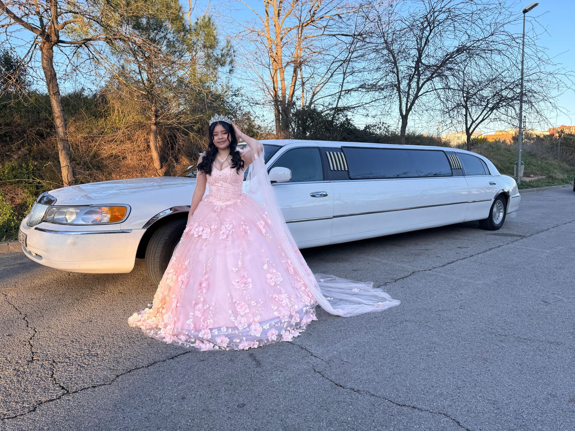 Una chica con un vestido rosa está parada frente a una limusina blanca.