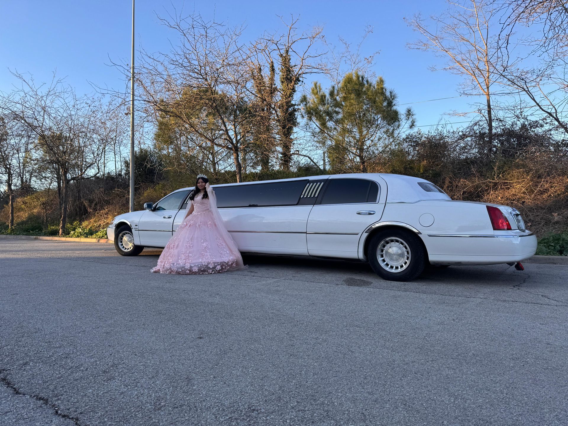 Una mujer con un vestido rosa está de pie junto a una limusina blanca.