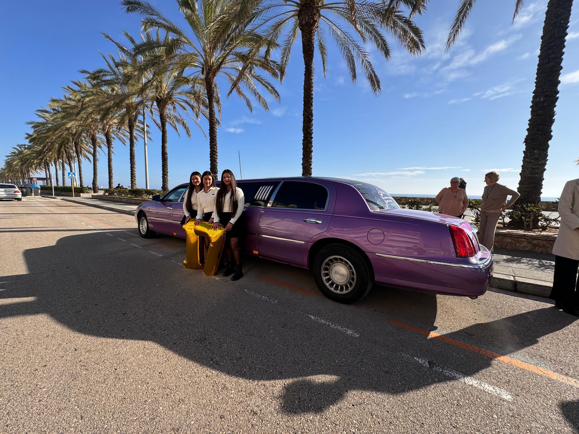 Tres mujeres están de pie junto a una limusina violeta.